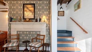 Una habitación con chimenea, sillas de madera, una mesita y una escalera con escalones azules.