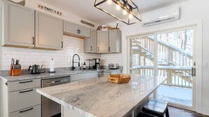 Una cocina con armarios blancos, encimera de mármol y un cesto de madera.