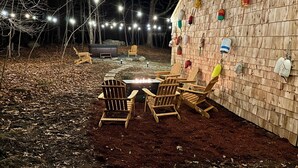 Un área de estar al aire libre con sillas de madera y un pozo de fuego, rodeada por un muro de madera decorado con diversos objetos.