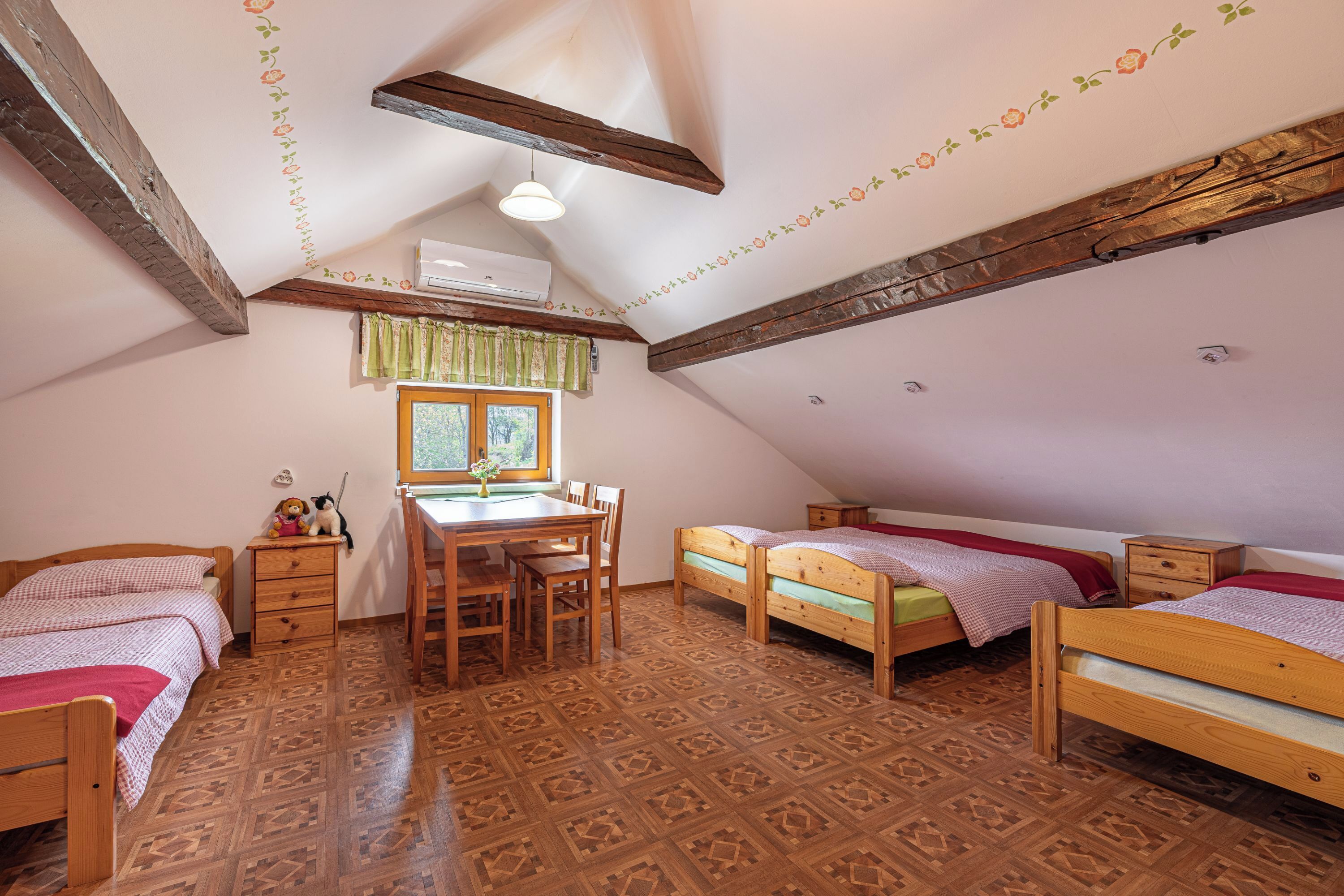 Un dormitorio acogedor en el ático con muebles de madera, una mesa de comedor y una ventana con cortinas.