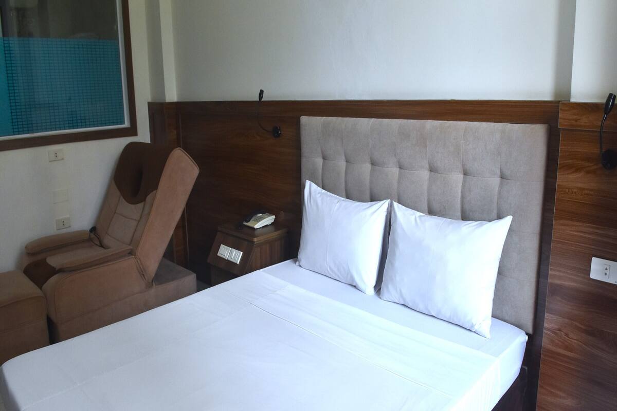 A hotel room with a large bed, a wooden headboard, a bedside table with a phone, and a chair.