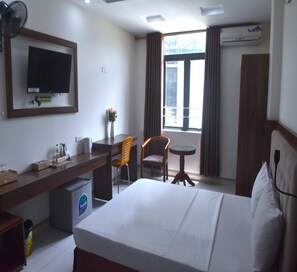 Une chambre d’hôtel équipée d’un lit, d’un bureau, d’une chaise, d’une petite table, d’un téléviseur et d’un appareil de climatisation.