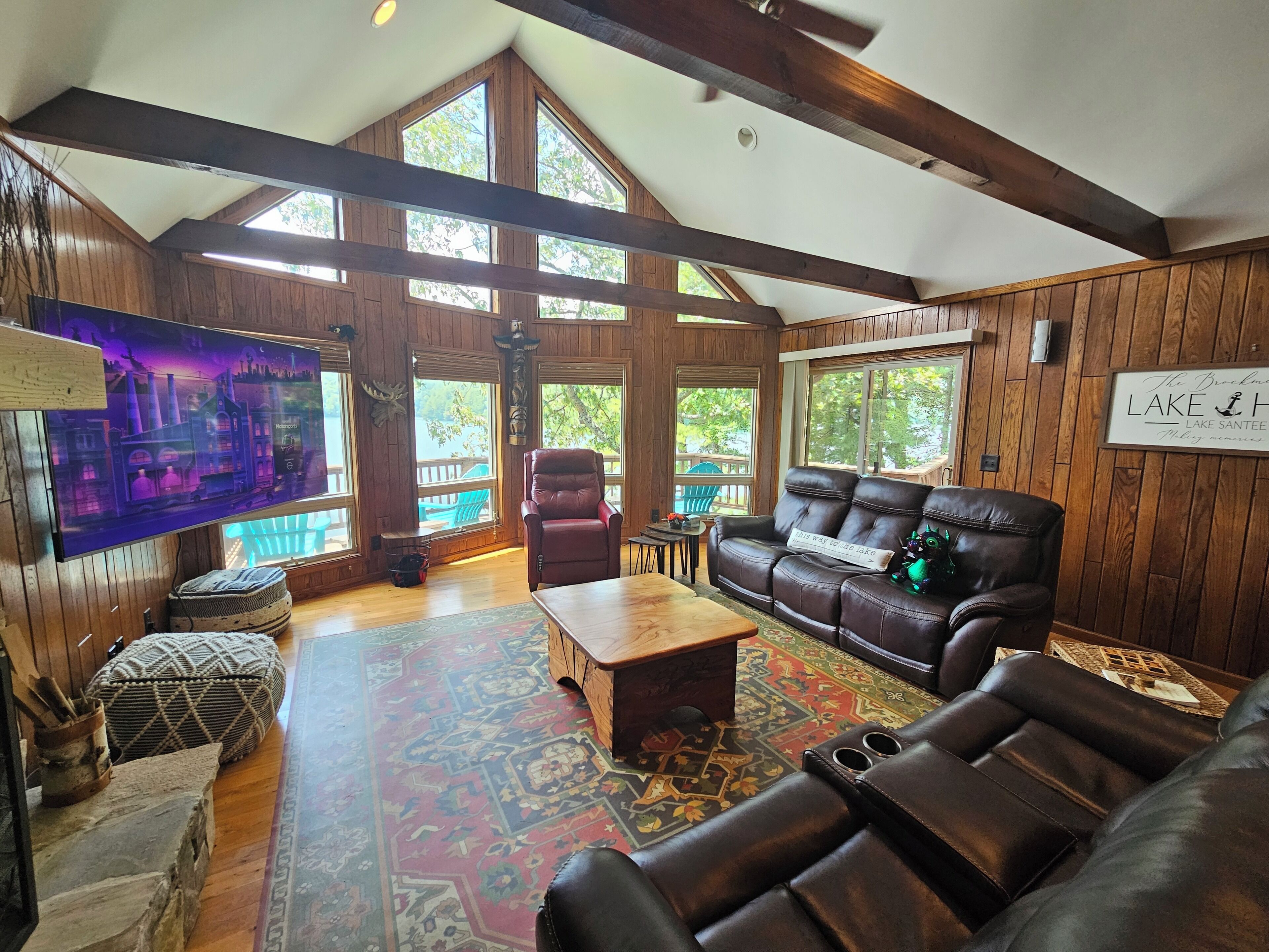 A spacious living room with a large wooden ceiling, a leather sofa, a coffee table, and a television mounted on the wall.