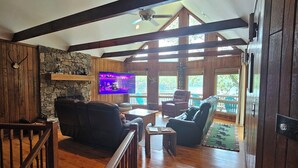 A spacious living area with a stone wall, wooden beams, a television, and a staircase.