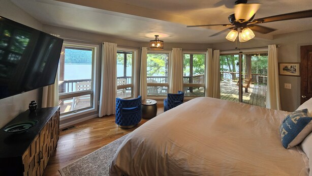 A bedroom with a large bed, a TV, and a view of a deck and lake.