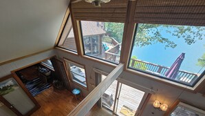 A spacious loft-style room with large windows, a wooden deck, and a view of a lake.