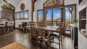 A spacious kitchen with wooden cabinets, a dining area with a large table and chairs, and a view of the outdoors through large windows. - Luxurious 4BD Near Canyons Village (Park City)
