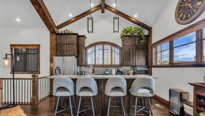 A kitchen with wooden cabinets, a large island with bar stools, a clock, and a window with a view. - Luxurious 4BD Near Canyons Village (Park City)