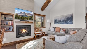 A modern living room with a fireplace, a large flat-screen TV, a sofa, and a bookshelf. - Luxurious 4BD Near Canyons Village (Park City)