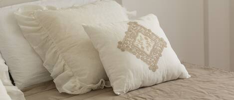 A bed with white pillows, one with a decorative embroidered design.