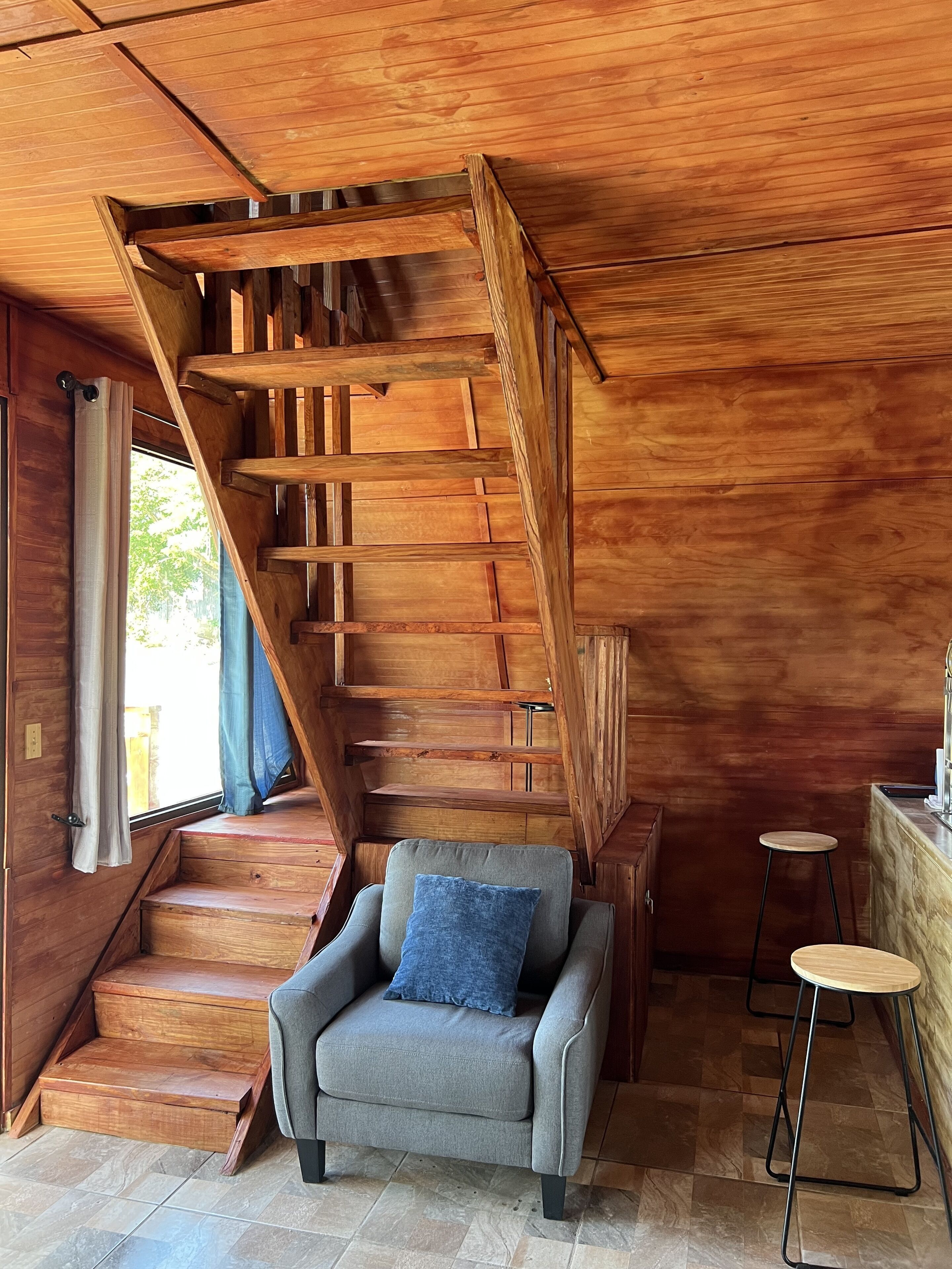 Eine Holztreppe führt zu einer Erkerzone mit einem grauen Sessel und einem kleinen Hocker.
