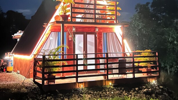 A triangular-shaped building with a balcony, a wooden fence, and a well-lit entrance. - Cabaña 787
Scape from reality in a cozy cabin
steps to a geological place. (Lares)