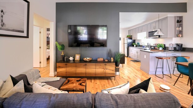 A modern living room with a large flat-screen TV, a wooden coffee table, and a sofa with multiple cushions. - ⁂10min-Airport⁂65"Smart Tv⁂W/D⁂Self Check-In⁂AC⁂DTSA⁂ (Santa Ana)