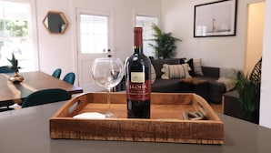 A wooden tray with a wine bottle and glass on a table in a well-lit room with a dining area in the background. - ⁂10min-Airport⁂65"Smart Tv⁂W/D⁂Self Check-In⁂AC⁂DTSA⁂ (Santa Ana)