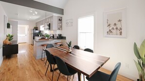 A modern kitchen with white cabinets, a wooden dining table, and black chairs. There is a large window providing natural light. - ⁂10min-Airport⁂65"Smart Tv⁂W/D⁂Self Check-In⁂AC⁂DTSA⁂ (Santa Ana)