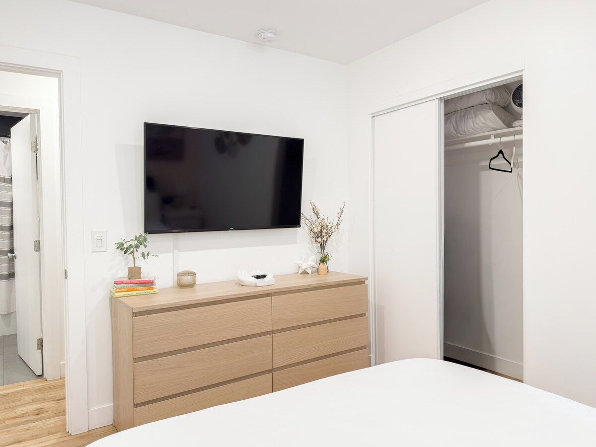 A bedroom with a bed, a dresser, a television mounted on the wall, and a closet.