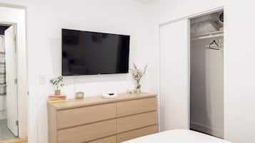 A bedroom with a bed, a dresser, a television mounted on the wall, and a closet.