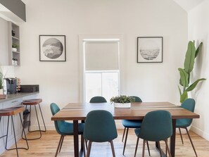Et spiseområde med et træbord og teal farvede stole, en plante til højre og to billeder i rammer på væggene.