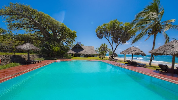 A swimming pool with a thatched-roof hut and palm trees in the background. - Amani Beach Resort (Kutani)