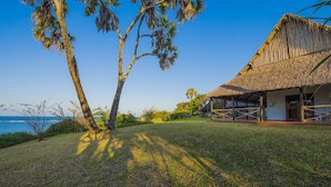 A thatched-roof house with a grassy lawn and palm trees. - Amani Beach Resort (Kutani)