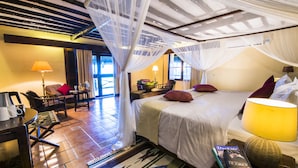 A hotel room with a bed, a desk, a chair, a lamp, and a window with curtains. - Amani Beach Resort (Kutani)
