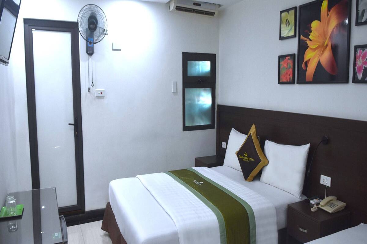 Une chambre d’hôtel avec un lit, une table de chevet et un ventilateur fixé au mur.