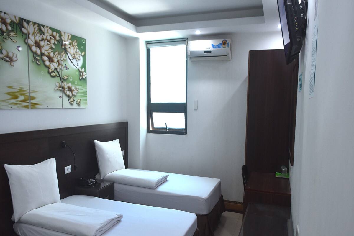 Une chambre d’hôtel avec deux lits, une télévision, un appareil de climatisation et une fenêtre.