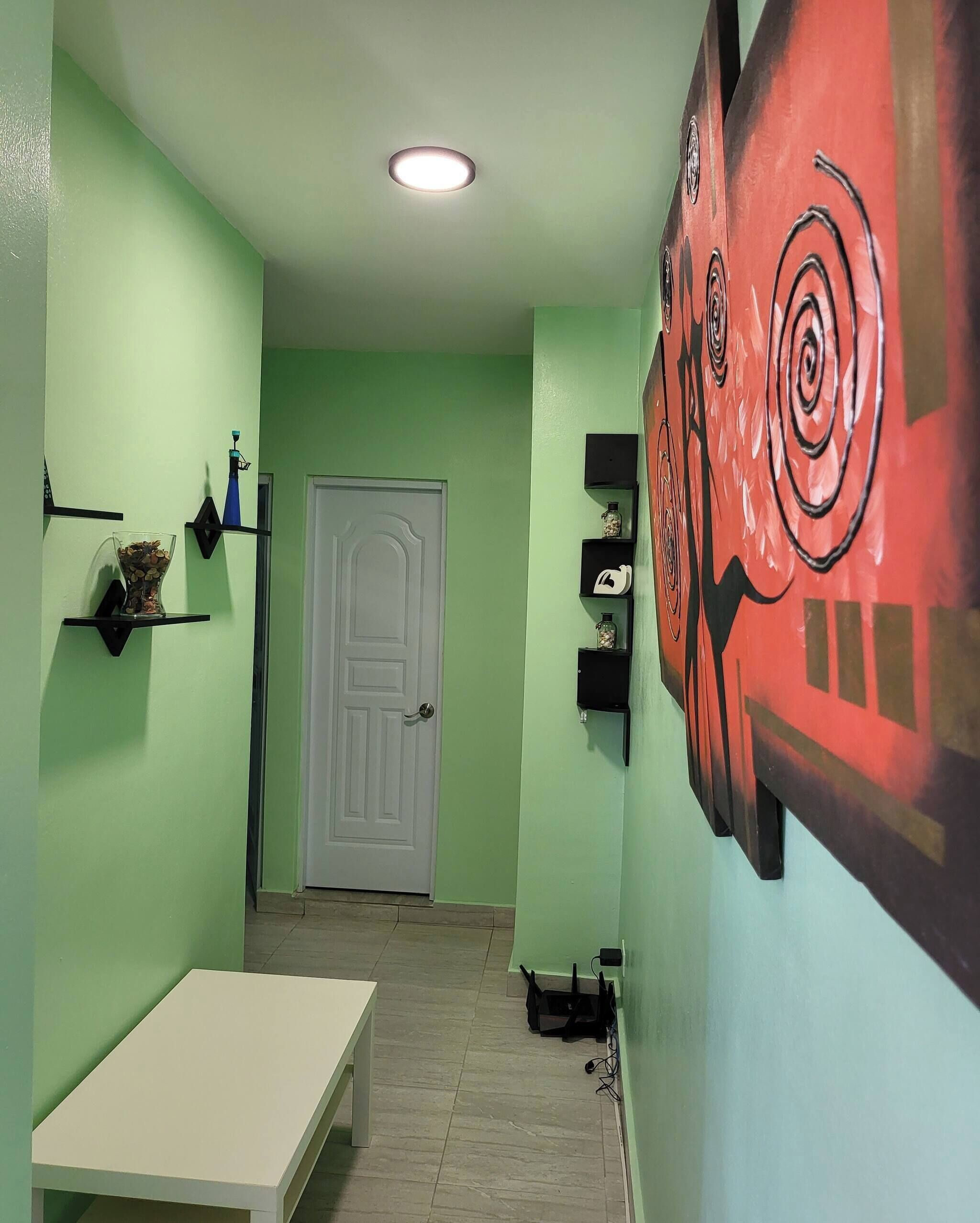 A narrow hallway with green walls, a white door at the end, and a large abstract painting on the right.