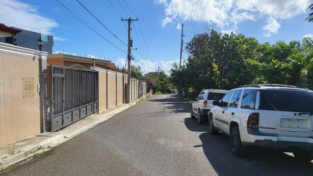 Una calle con coches estacionados y un edificio con reja.