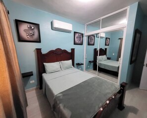 Ein Schlafzimmer mit Bett, Kleiderschrank, Spiegel und Klimaanlage.