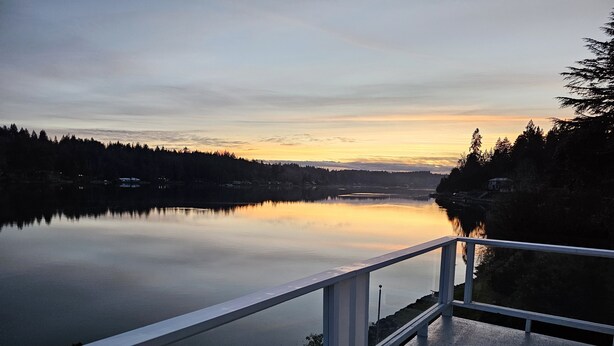 A calm lake at sunset with a wooden deck and railing. - 180' private beach and spacious entertainment oasis on Hammersley Inlet for 8! (Shelton)