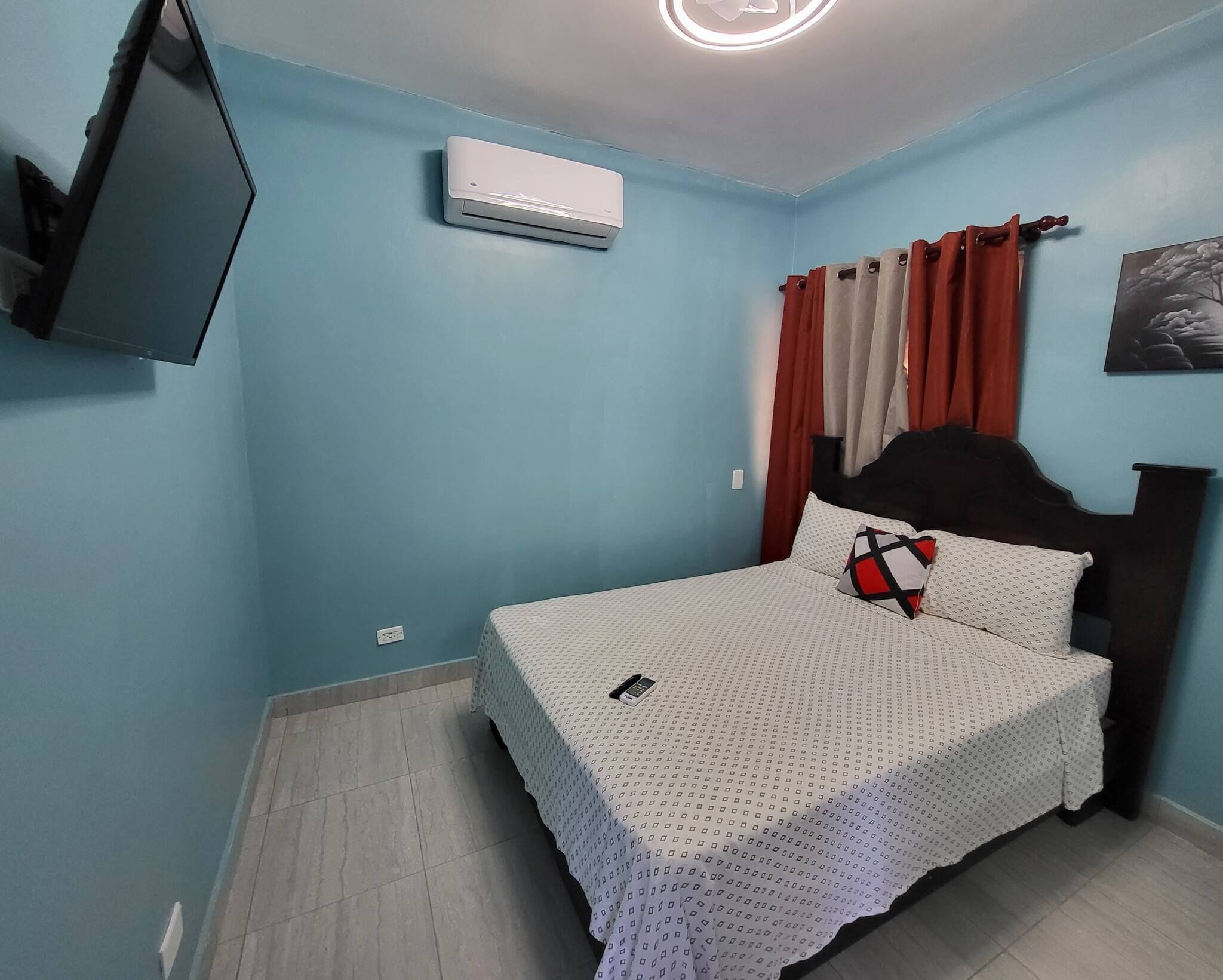 A bedroom with a bed, a TV mounted on the wall, an air conditioner, and a curtain.