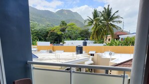 Un balcon avec deux fauteuils en osier, une vue sur un quartier résidentiel et une montagne en arrière-plan.