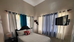 Une chambre à coucher avec un lit, des rideaux, une télévision et une lampe.
