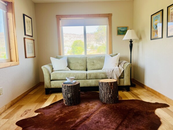 A living room with a green sofa, two wooden stools, a brown rug, and a lamp. - River Front Cabin. Come relax and play cowboy in Spray ! (Spray)