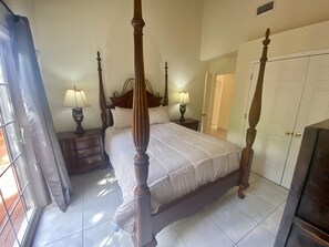 A four-poster bed with a wooden frame, two bedside tables with lamps, a wardrobe, and a door leading to another room.