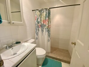 A bathroom with a toilet, sink, and shower curtain. - Tropical Caribbean Oasis (Jolly Harbour)