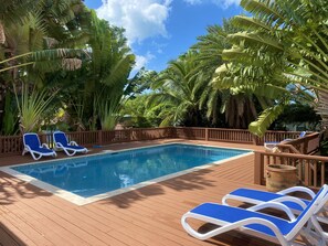 A swimming pool with wooden deck and lounge chairs, surrounded by tropical foliage.