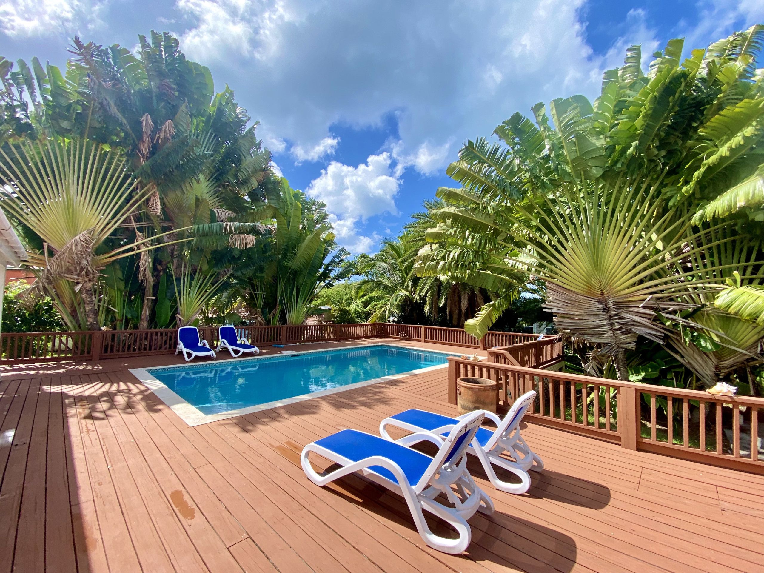 Eine Holzterrasse mit Pool und Liegestühlen.