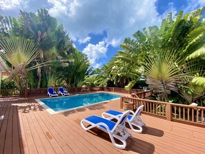 Una terraza de madera con piscina y sillones de descanso.