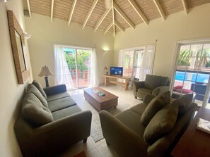 A spacious living room with a high ceiling, a large window, and a view of a pool.