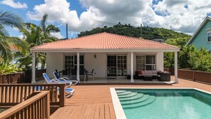 A poolside area with a covered seating area, lounge chairs, and a view of a hill.
