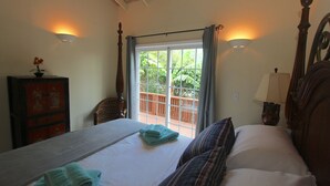 Une chambre à coucher comprenant un lit, une table de chevet, une lampe, une fenêtre avec des rideaux et une vue sur un balcon.
