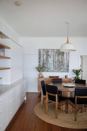 A dining area with a round wooden table, black chairs, a woven rug, and a pendant light.