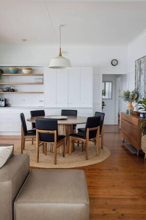 A modern kitchen with white cabinets, a round wooden dining table, and black chairs. - Sea Cliff Sands Gerroa (Gerroa)