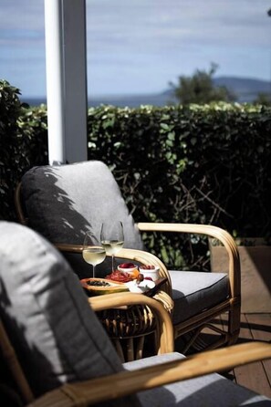 A wicker chair with cushions, a glass of white wine, and a plate of food on a terrace with a view of the sea. - Sea Cliff Sands Gerroa (Gerroa)