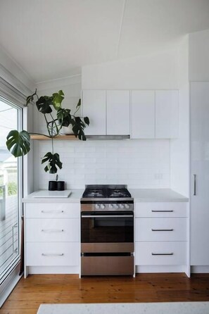 A modern kitchen with white cabinetry, a stainless steel oven, and a potted plant. - Sea Cliff Sands Gerroa (Gerroa)