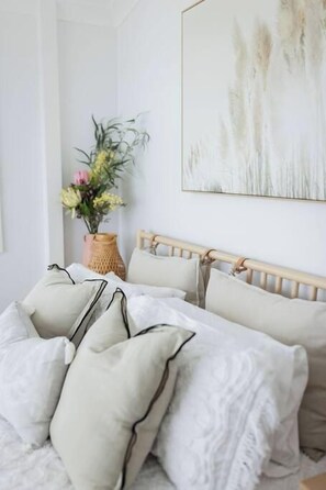 A neatly made bed with a wooden headboard, a bedside plant, and a framed artwork on the wall. - Sea Cliff Sands Gerroa (Gerroa)