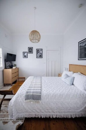 A bedroom with a bed, a bedside table, a dresser, and a hanging light fixture.