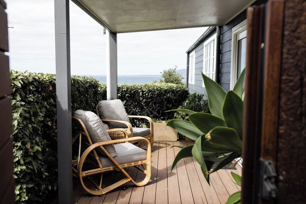 A covered outdoor area with a wicker chair, a potted plant, and a view of the sea.